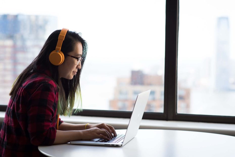 junge Frau mit Kopfhörer sitzt vor Laptop