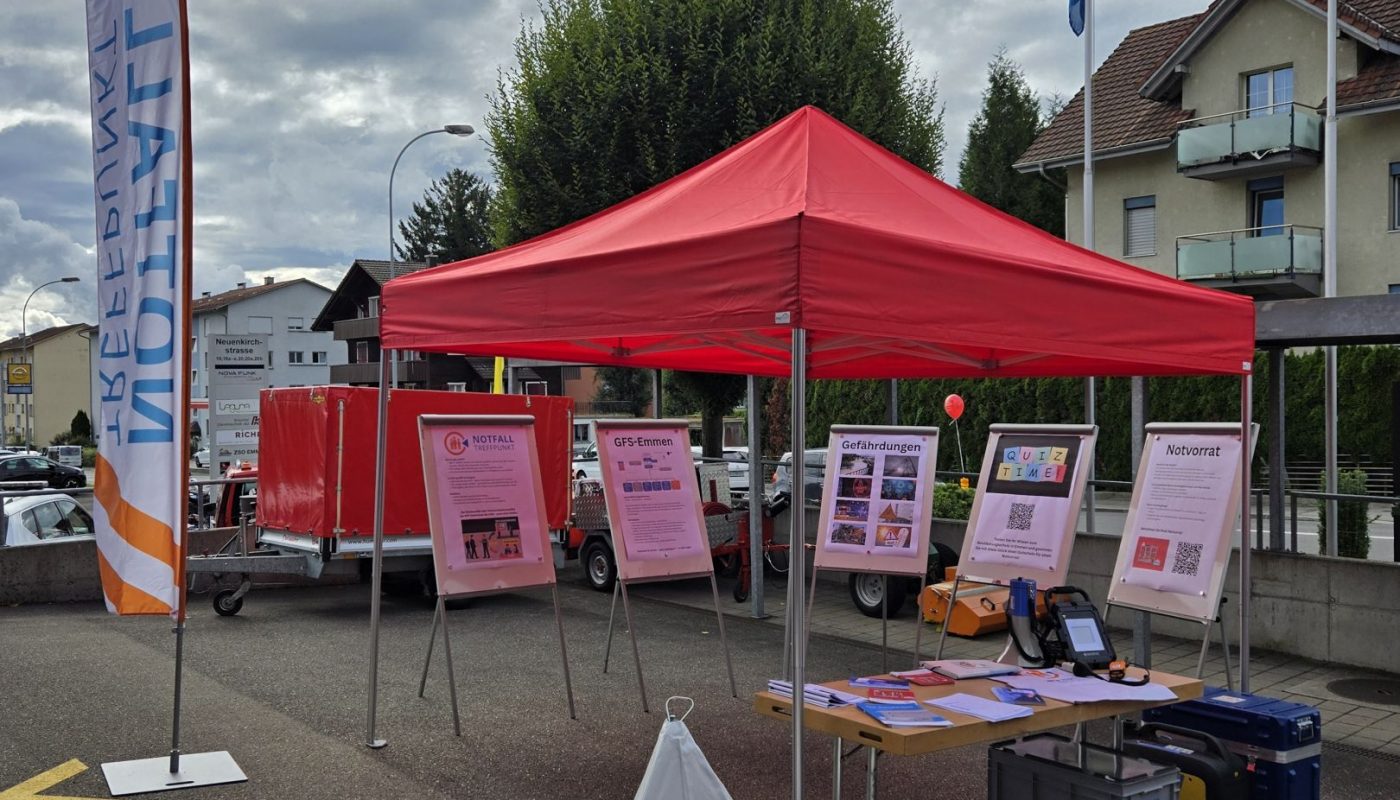 Informationsstand Bevölkerungsschutz Emmen mit rotem Zelt, Infotafeln, Notfalltreffpunkt-Schild und Materialien zum Thema Krisenvorsorge.
