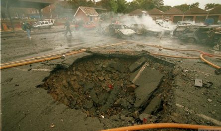 Bild eines Bombenkraters auf einem asphaltierten Platz von mehreren Metern Durchmesser und Tiefe.
