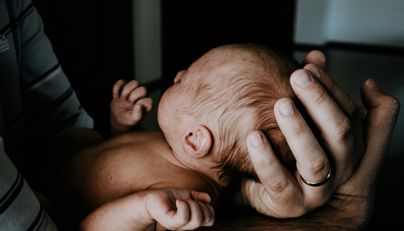 Ein Baby liegt geborgen in den Händen seines Vaters.