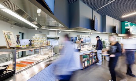 Mehrere Gäste bewegen sich durch ein modernes Selbstbedienungsrestaurant mit offenen Ausgabestationen und Buffettheken.