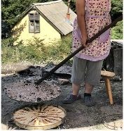 Fli wird traditionell am Feuer zubereitet in einem Dorf mit einem Haus im Hintergrund und einer Frau die kocht