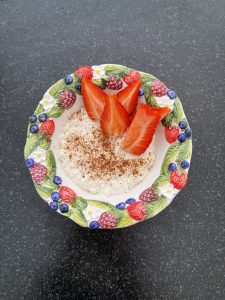 Milchreis in einer Schüssel mit Erdbeeren, Heidelbeeren, Himbeeren und Zimt