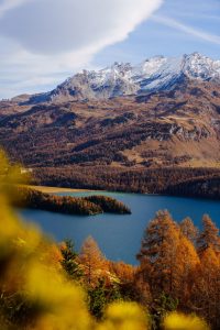 Klarer, blauer See im Herbst im Engadin (Graubünden, Schweiz). Im Hintergrund majestätische Berge, deren Spitze mit Schnee bedeckt ist. 