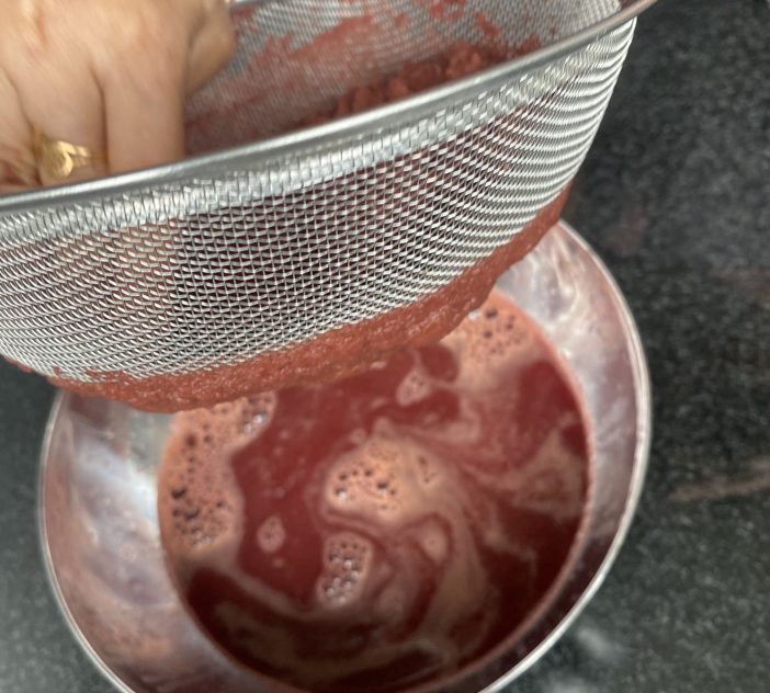 A bowl with red juice in it poured through a sieve.