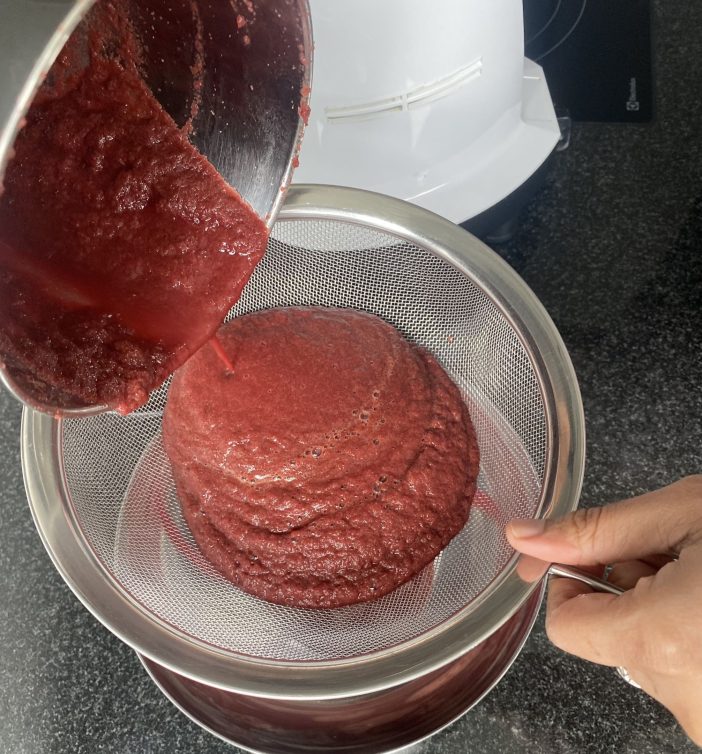 An image depicting red solid juice being poured through a sieve.
