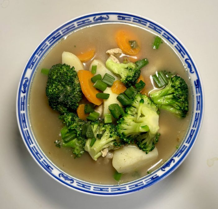 Healthy clear chicken soup with carrots, potatoes, and broccoli in a white bowl, perfect for boosting immunity and nourishing the body.