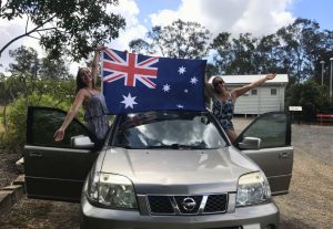 Two girls standing on a car waving an Australian flag.