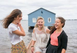 Three girls laughing together in front of the blue boat house in Perth, Australia