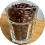 A clear glass cup filled with medium roast coffee beans, highlighting rich aroma and quality for espresso brewing.