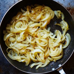 Golden caramelized onions cooking in a skillet, a key topping for traditional Argentine fugazza pizza, adding sweetness and depth to this iconic Buenos Aires dish.
