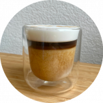 "Clear glass cup of espresso with milk, showing creamy layers.