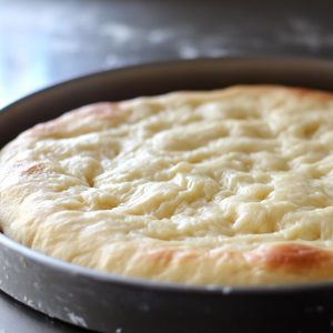 Thick, airy fugazza dough pressed into a round baking pan, ready for pre-baking as the base for traditional Argentine onion pizza from Buenos Aires.