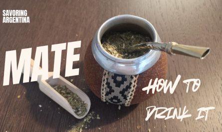 Top-down view of a traditional Argentine mate gourd filled with yerba mate and a metal bombilla straw, with a wooden scoop and scattered leaves on a table. Text overlay reads “Mate – How to Drink It” as part of the Savoring Argentina series.