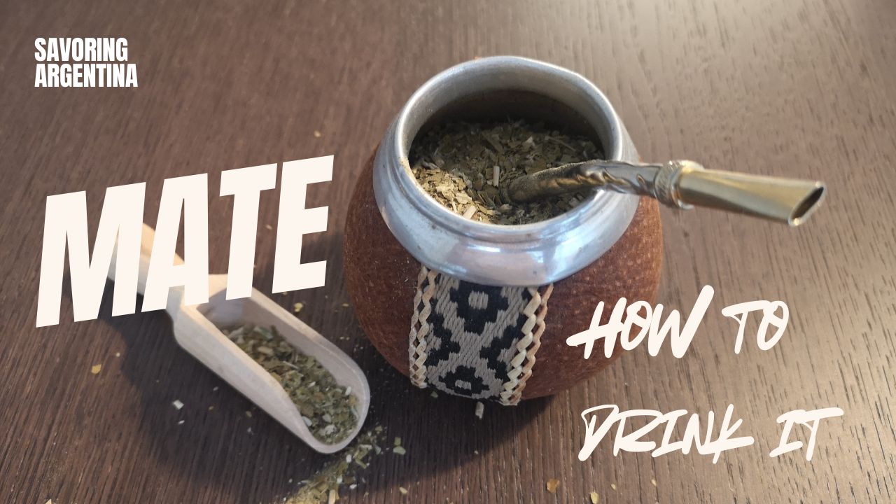Top-down view of a traditional Argentine mate gourd filled with yerba mate and a metal bombilla straw, with a wooden scoop and scattered leaves on a table. Text overlay reads “Mate – How to Drink It” as part of the Savoring Argentina series.