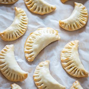 Unbaked empanadas arranged on parchment paper, sealed with forked edges and ready for the oven.